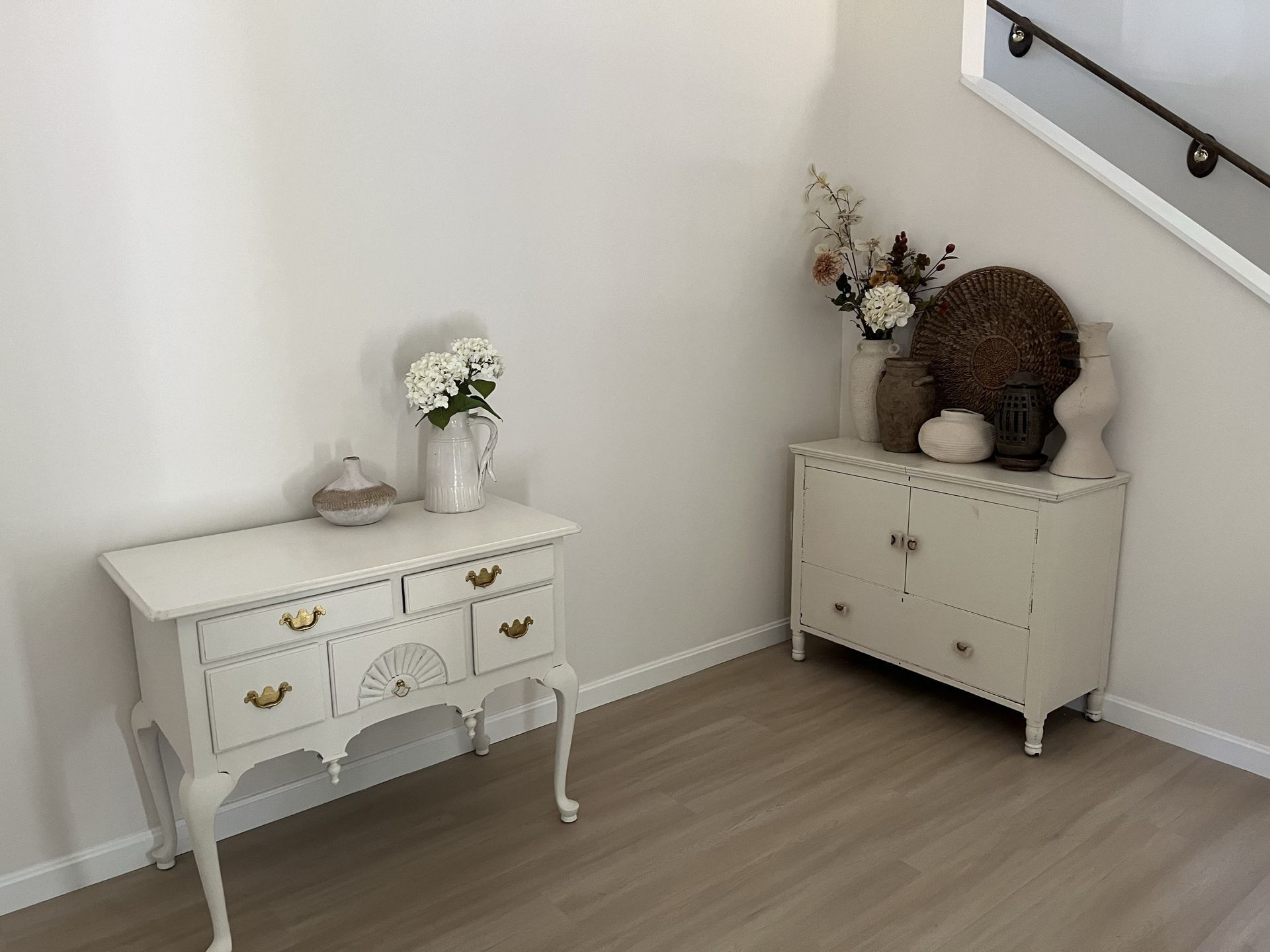 A white dresser with a vase of flowers on top of it in a room next to a staircase