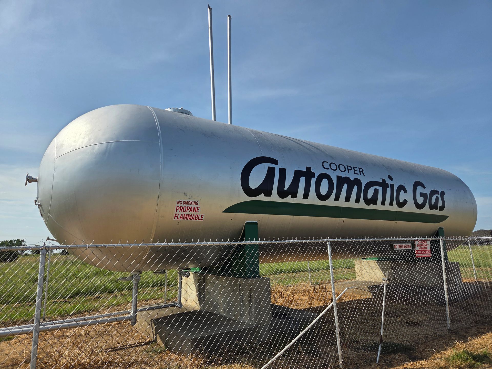 Rows of silver cylindrical tanks with black domes parked in an outdoor lot, with a pickup truck and building behind.