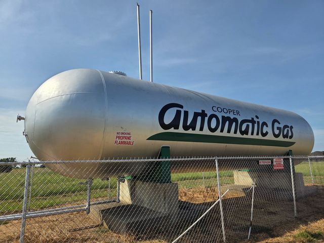 Rows of silver cylindrical tanks with black domes parked in an outdoor lot, with a pickup truck and building behind.