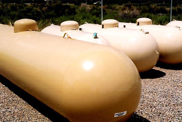 Row of large tan propane tanks on gravel in an outdoor storage yard