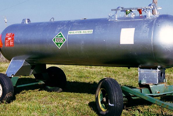 Blue horizontal fuel tank on a wheeled trailer sitting on grass outdoors