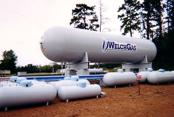 Large white Welch Gas propane tanks in an outdoor storage yard with trees in the background