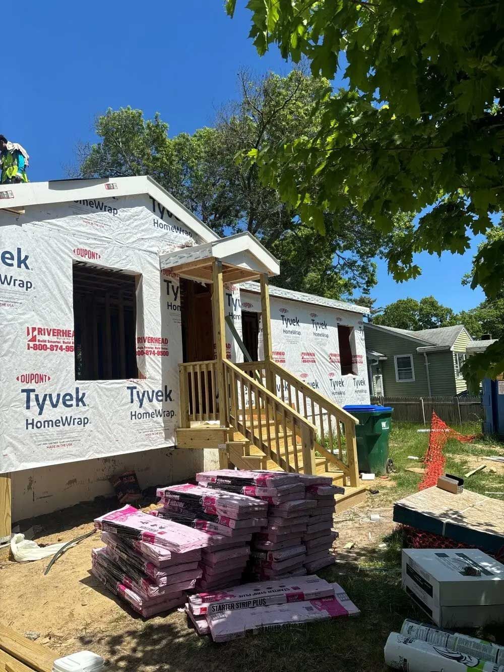 Construction site of a small house under development; Tyvek wrap, wooden porch with stairs, pink insulation.