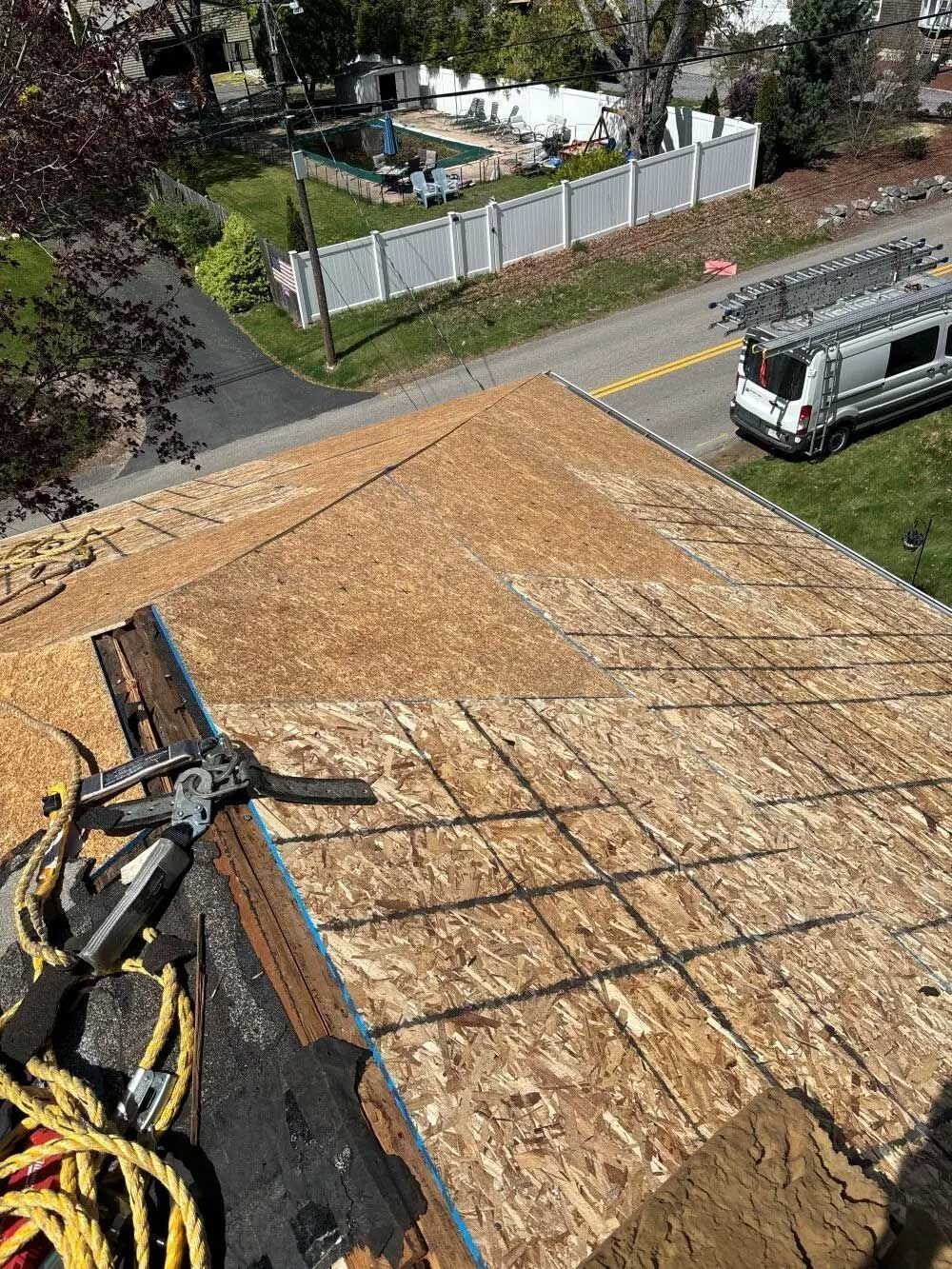 Rooftop partially torn up with tools and safety equipment. A road and houses are in the background.