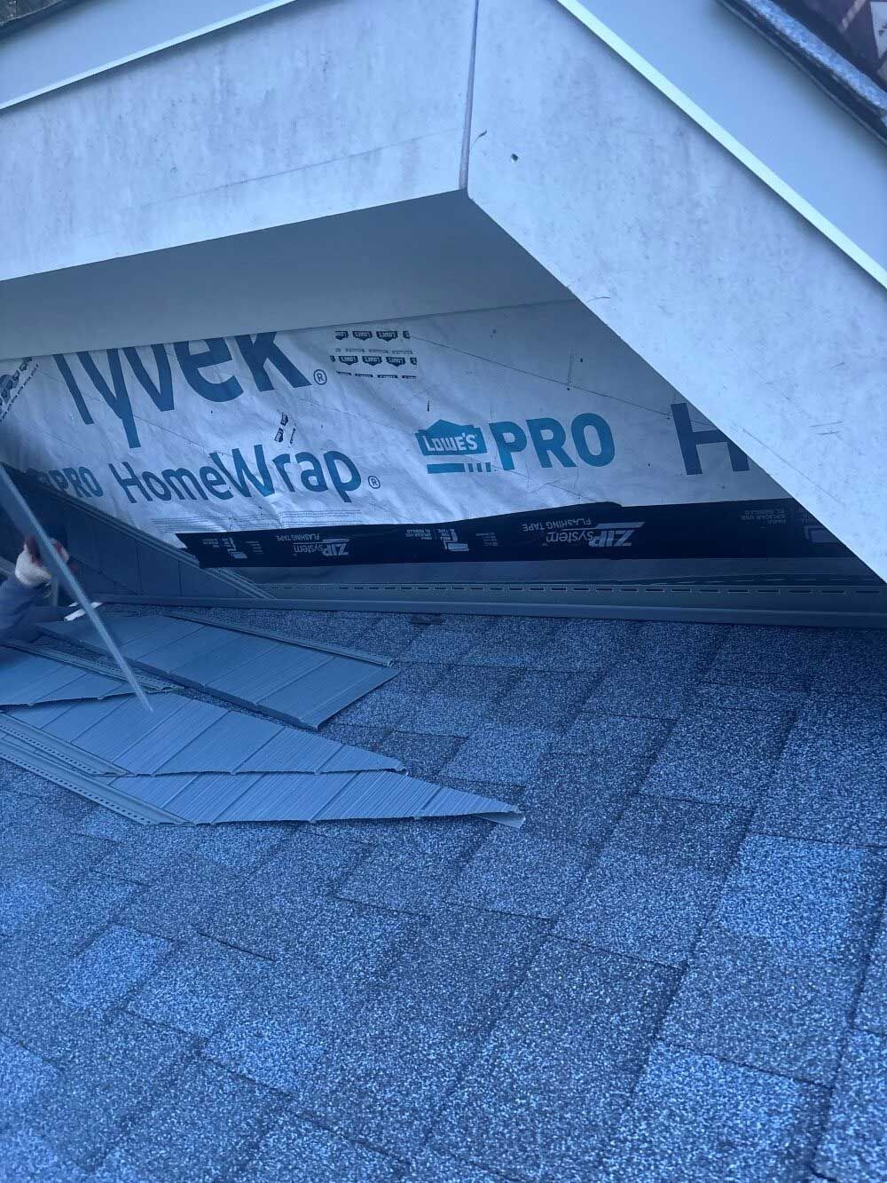Roof with exposed Tyvek wrap. A person works on installing shingles.