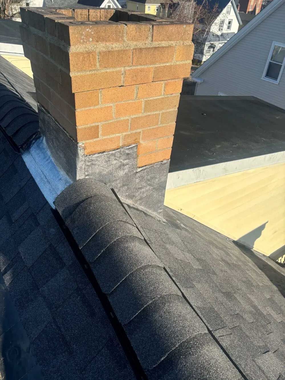 Chimney on a shingled roof with flashing; brick and gray shingles.