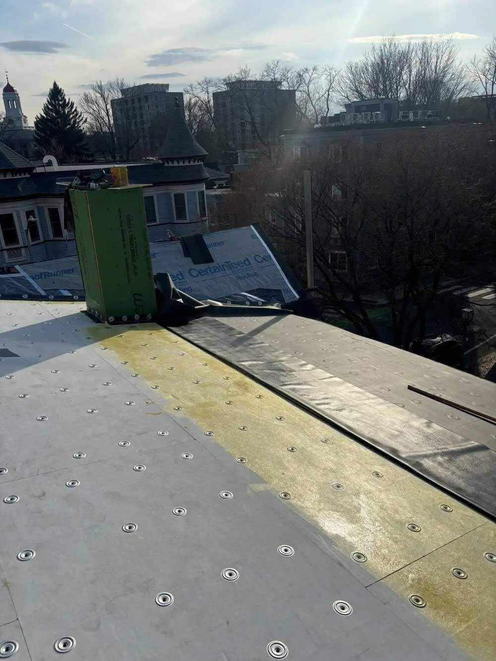 Rooftop view with gray and yellow insulation, black sealant, and buildings in the background.