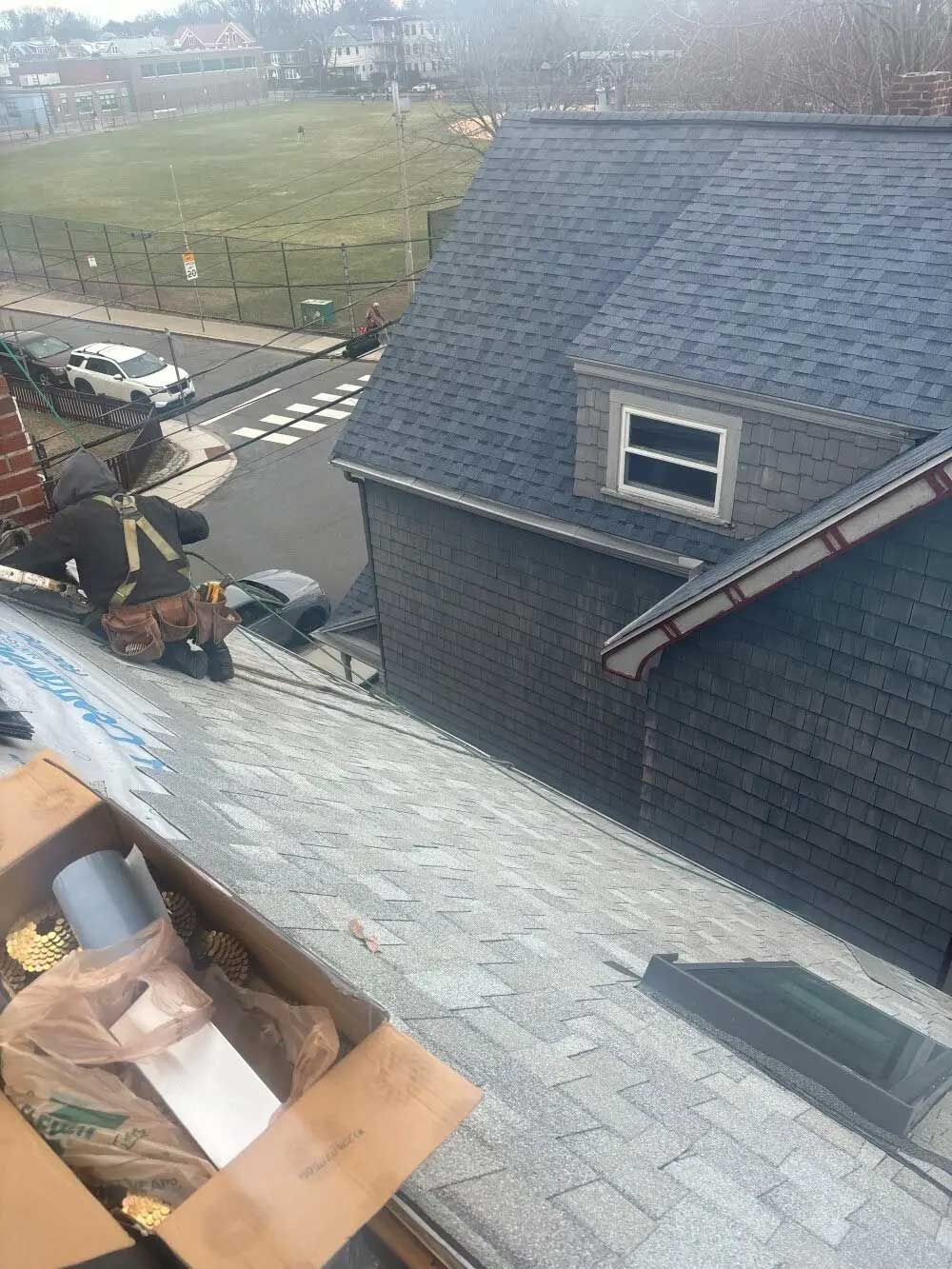 Roofer working on a house roof with gray shingles and a small dormer. Sunny day.