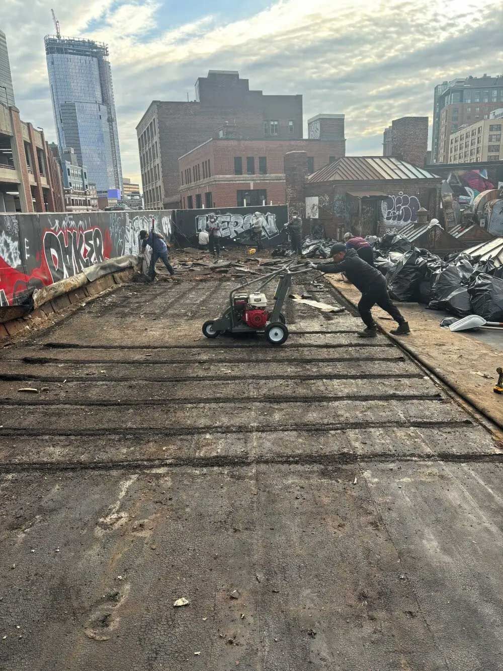 People removing old asphalt from a street using a lawnmower in an urban setting.