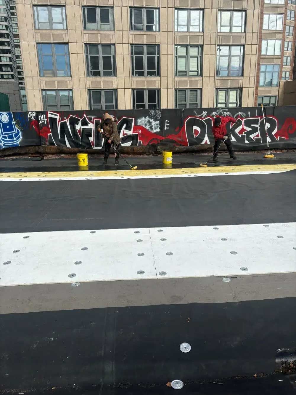 Two people spray painting graffiti on a wall, with a building backdrop.
