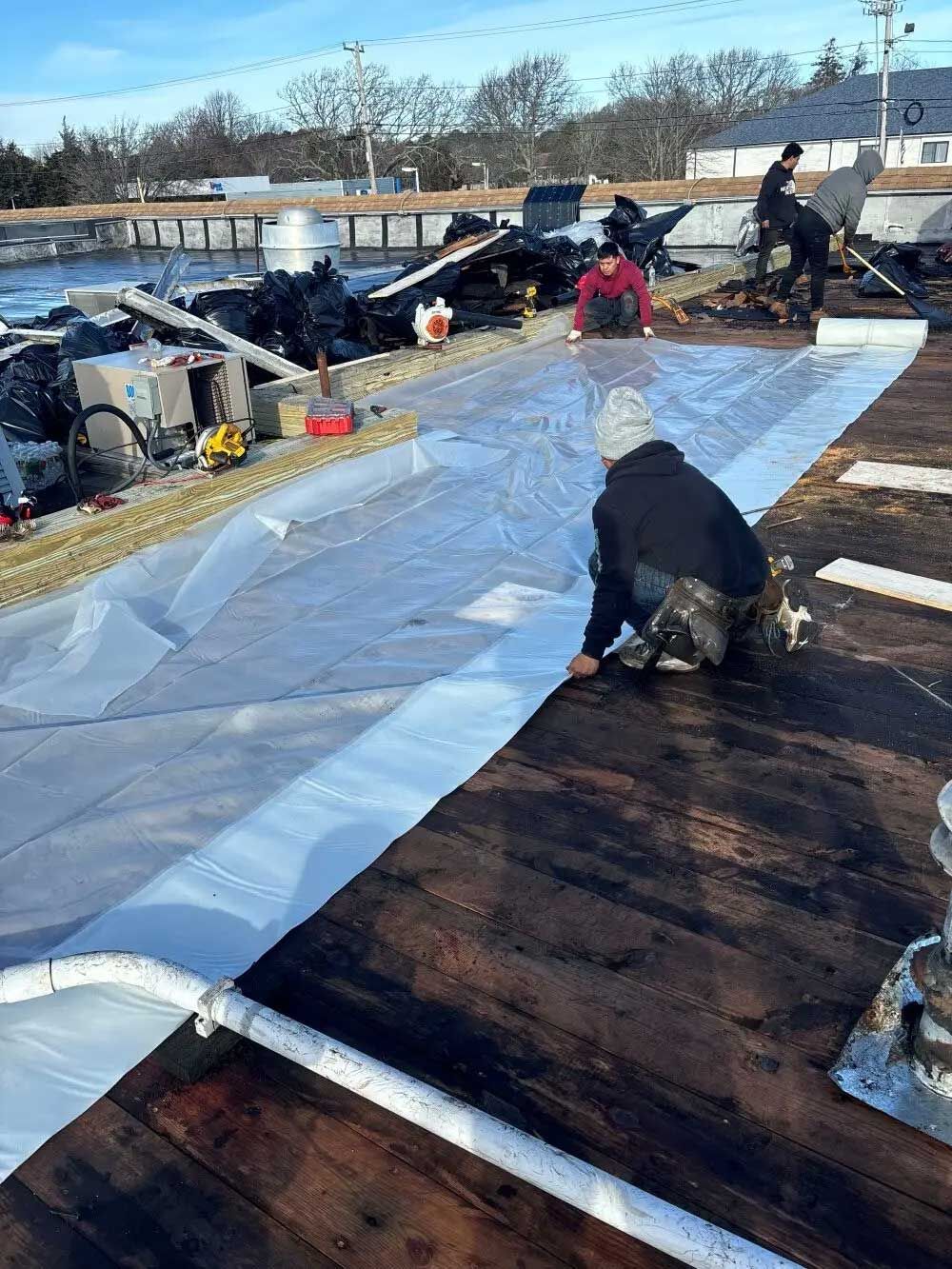 Construction workers installing roofing on a rooftop. White material being laid down with a clear blue sky.