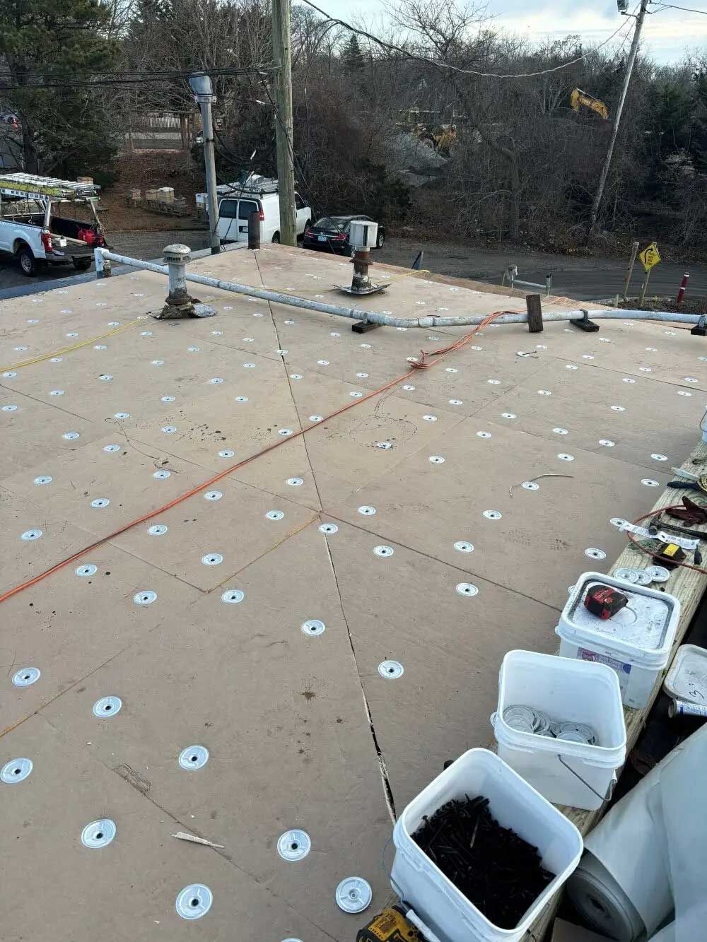 Rooftop with new construction; many white washer discs; buckets and tools; truck parked nearby.