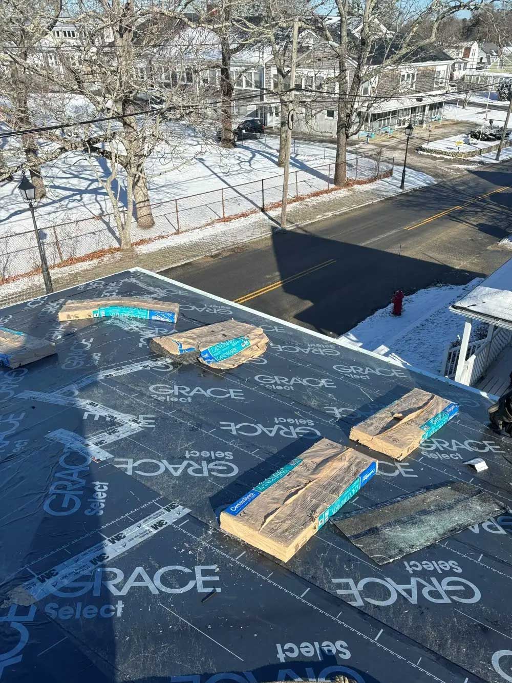 Rooftop covered with dark waterproof underlayment, wooden supports. Street in background. Winter scene.