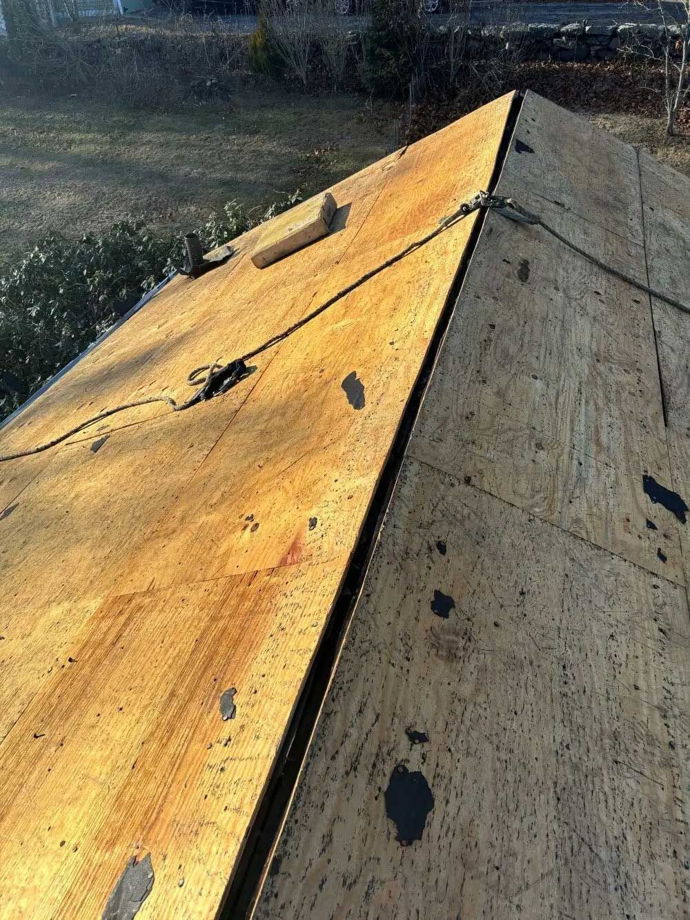Close-up of a roof with aged, weathered plywood, showing the ridge, with exposed materials and dark patches.