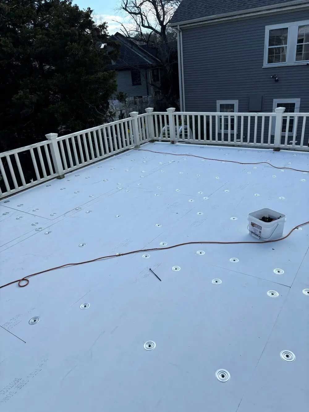 A gray deck with white railings and a house in the background. Fasteners are visible on the deck.