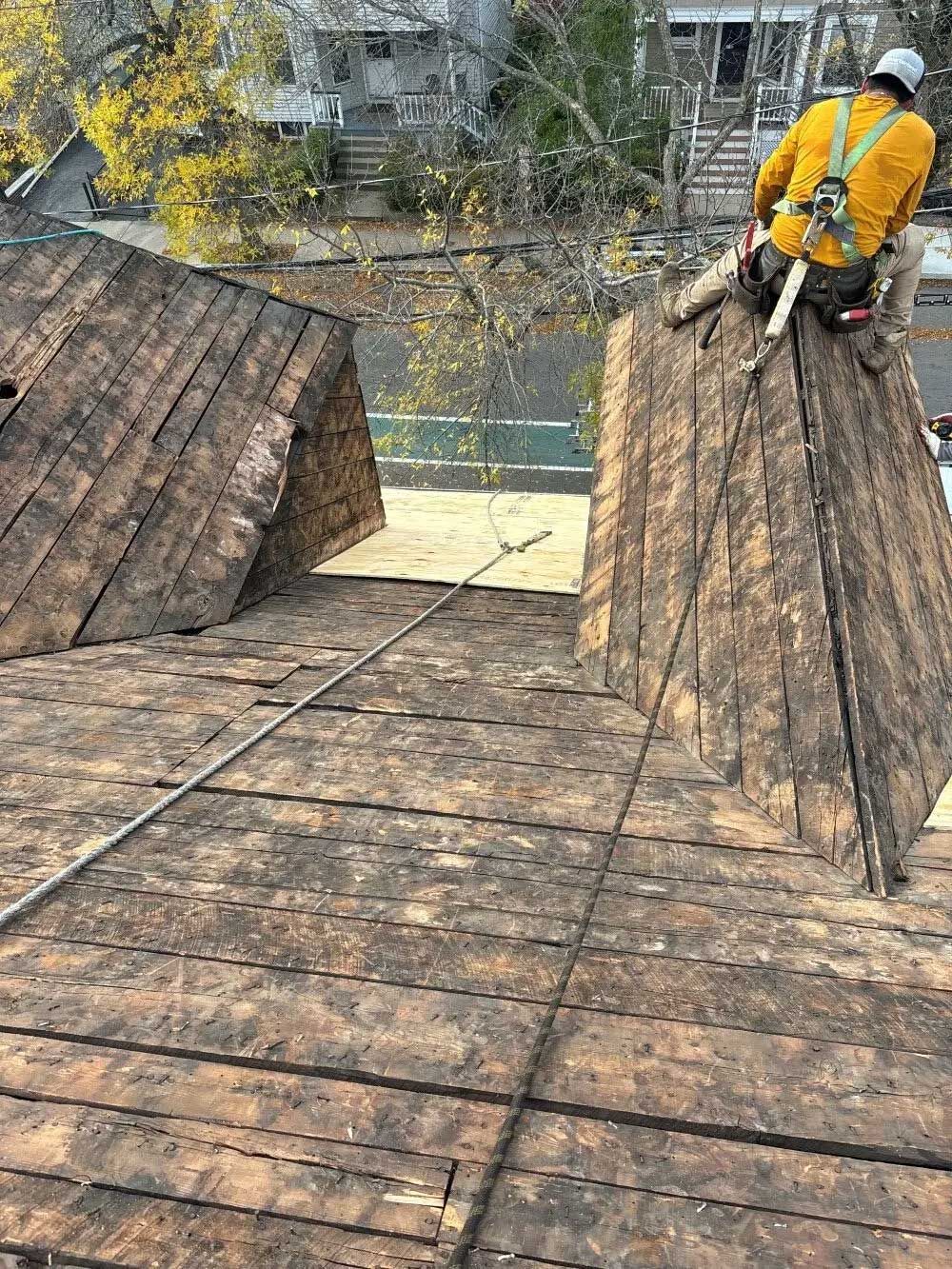 Roofer in yellow jacket on a weathered roof, using safety harness.