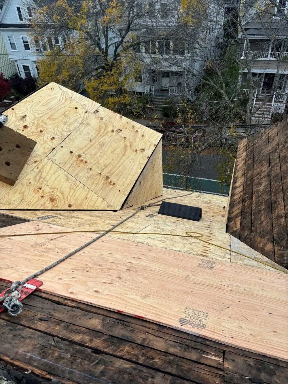 Rooftop with plywood installation; work in progress. Safety harness in use. Outdoors, fall season.