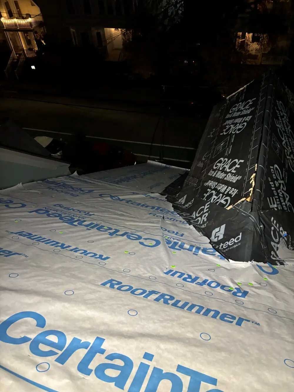 Rooftop with waterproof roofing material, black tarp tent, and a person, at night.