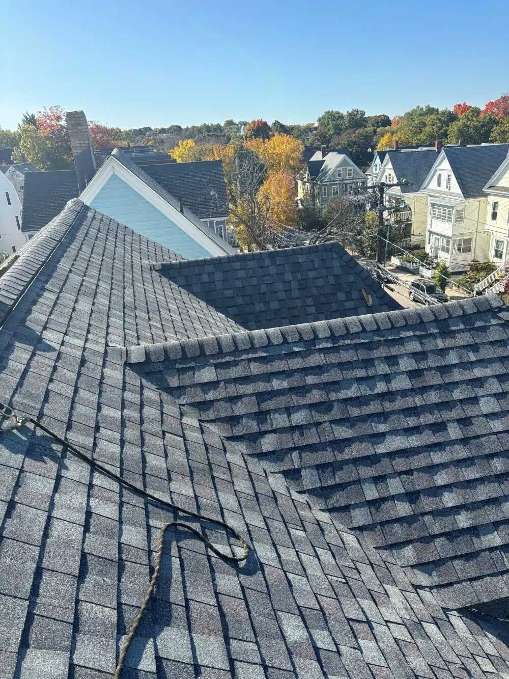 Rooftop view of gray shingled roofs with trees in the background under a clear blue sky.