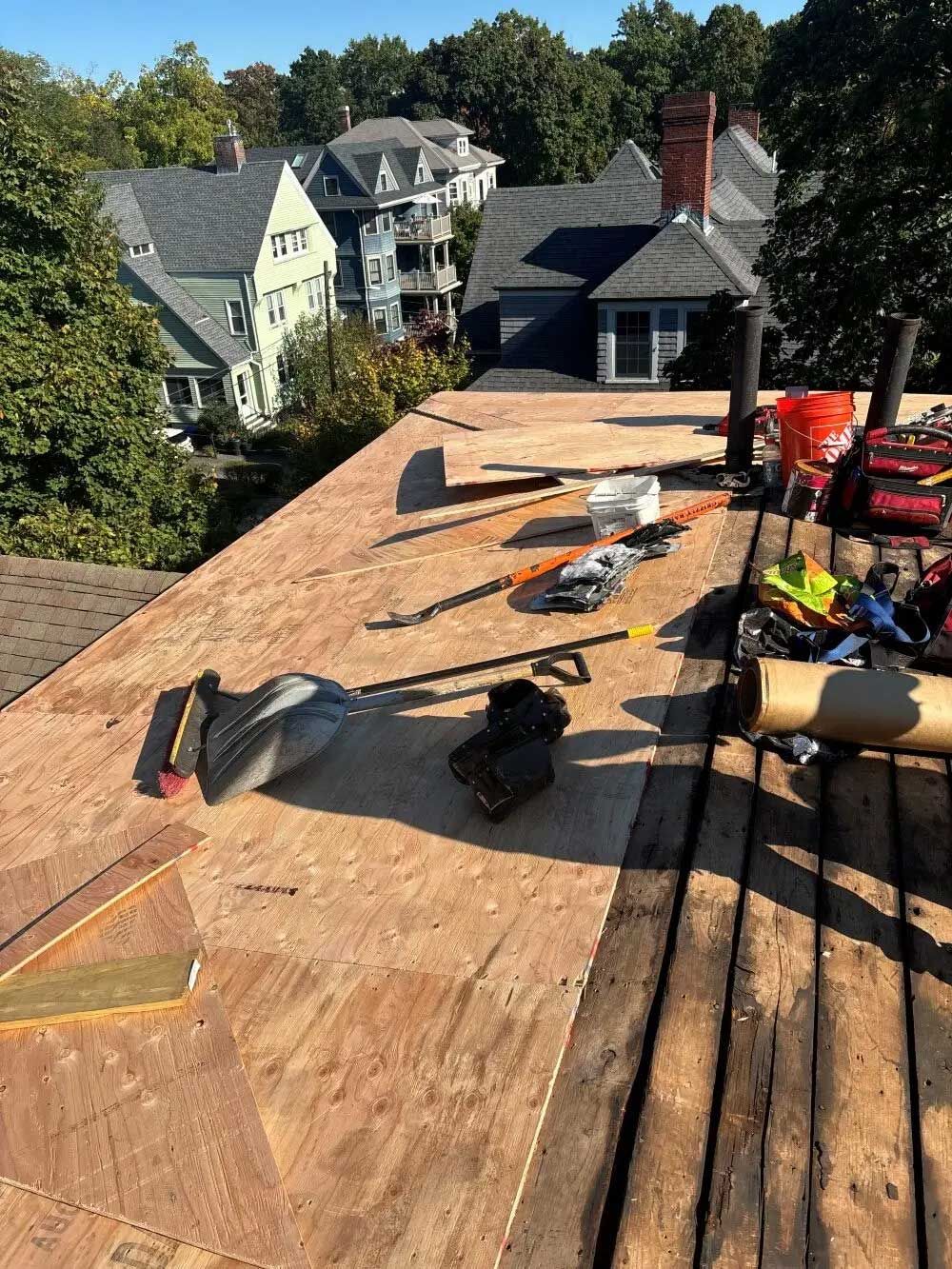 Construction materials and tools on a flat rooftop, likely for roof repair, with houses in the background.