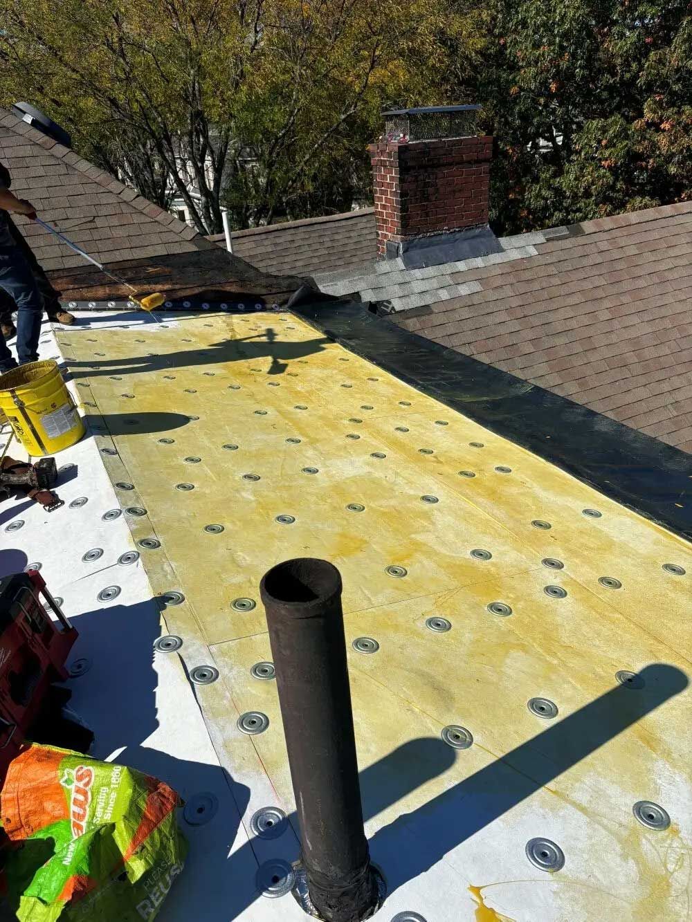 Rooftop scene; a section of roofing under repair, with a chimney, vent pipe, and tools visible.