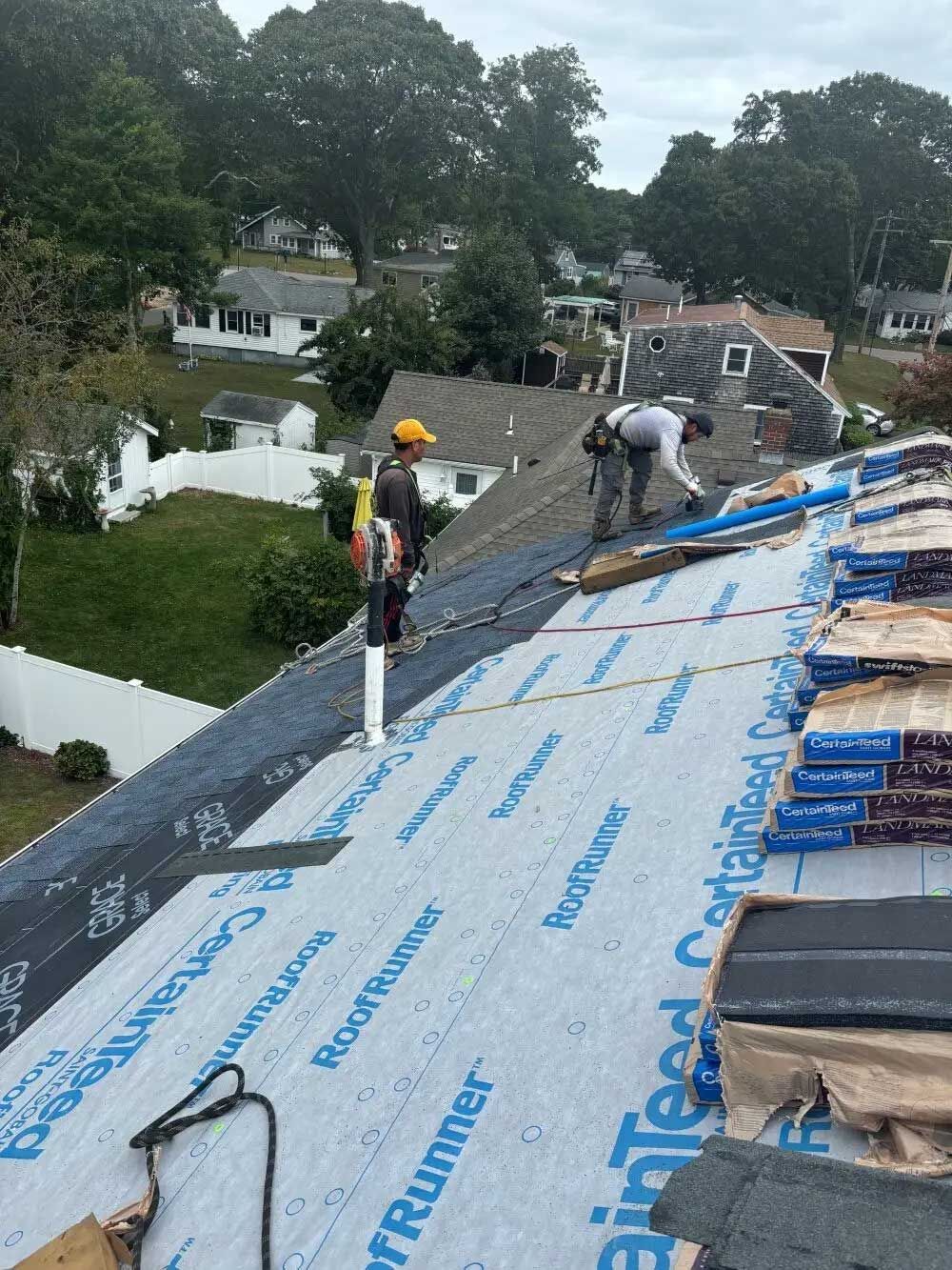 Roofers installing shingles on a residential rooftop, cloudy sky overhead.