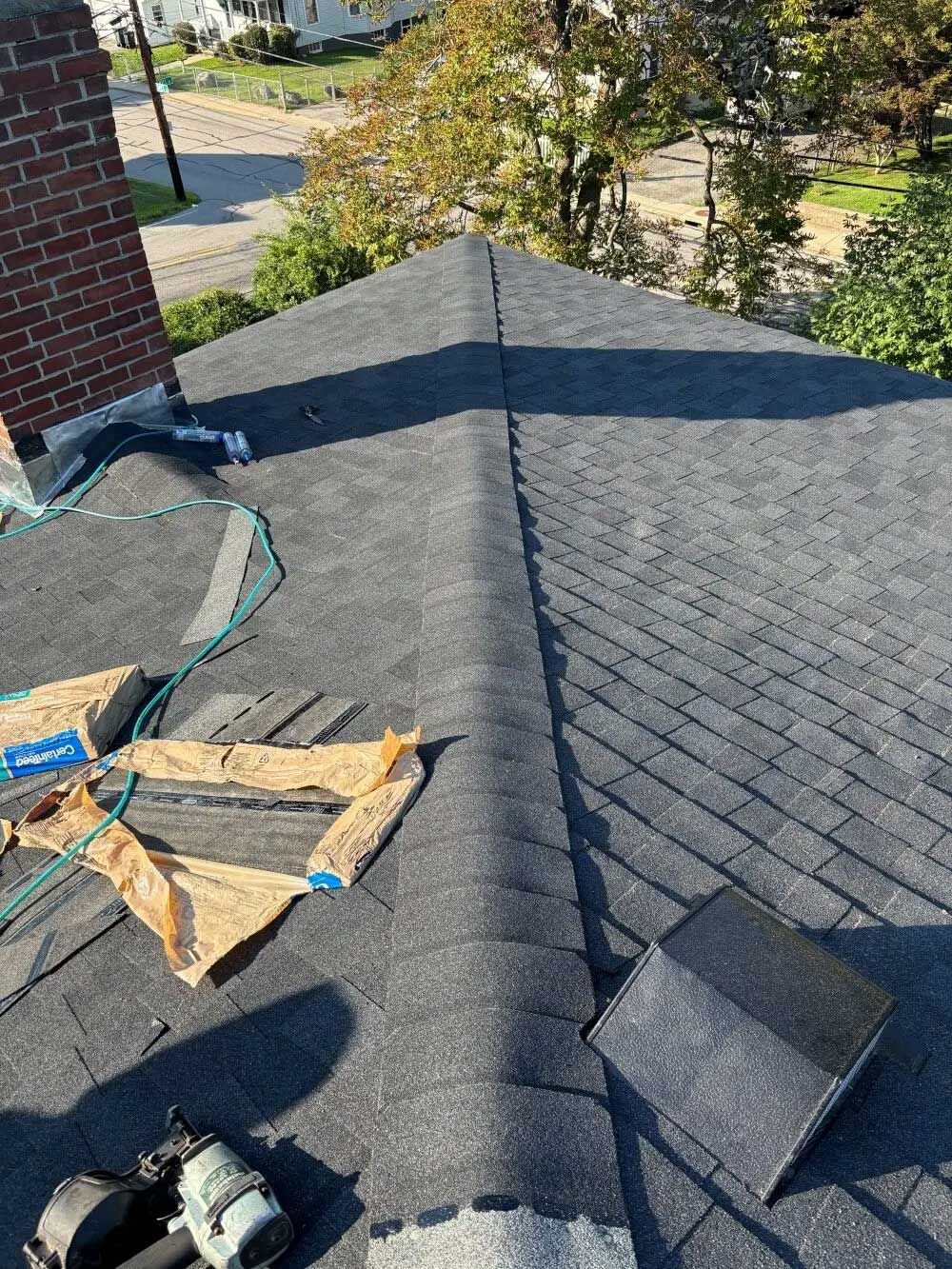 Asphalt shingle roof with a brick chimney and tools; outdoor shot.