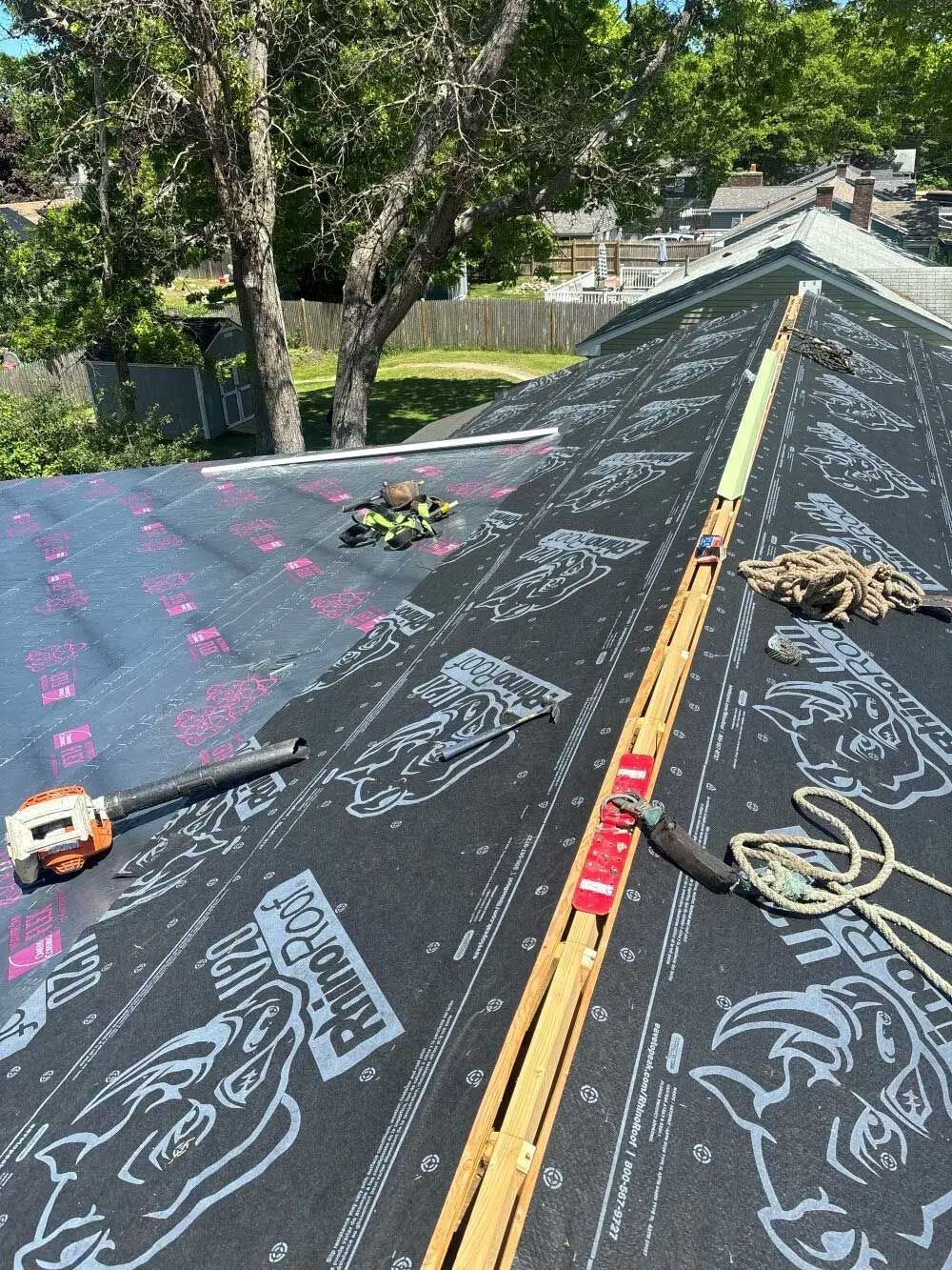 Roof with new underlayment, tools, and safety rope, being worked on outside on a sunny day.