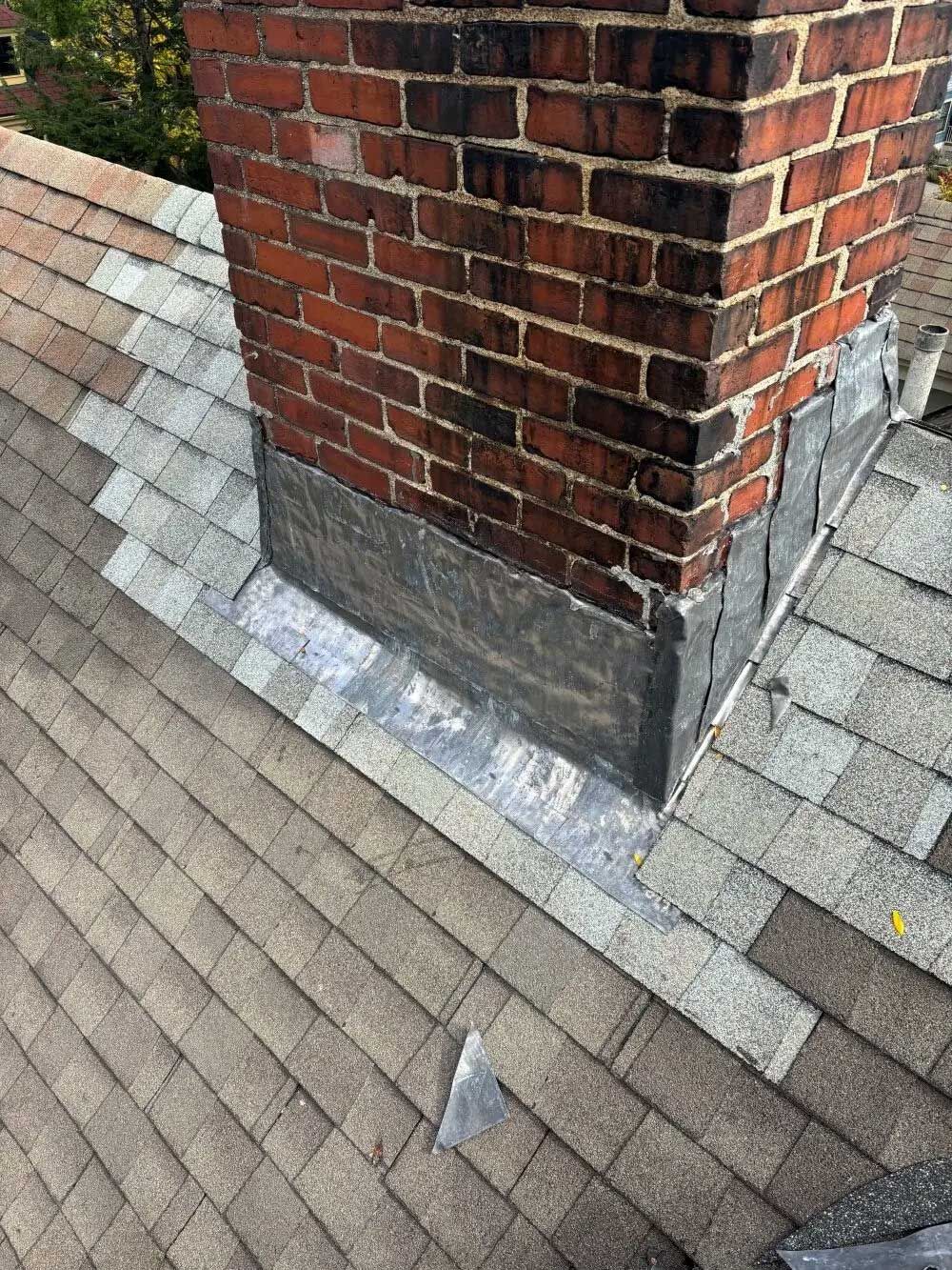 A brick chimney with lead flashing on a shingle roof.