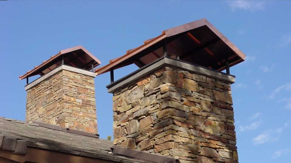 Two stone chimneys with copper-roofed caps against a blue sky.