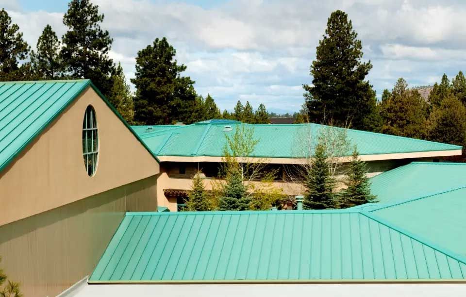 Buildings with turquoise roofs surrounded by green trees and a cloudy sky.