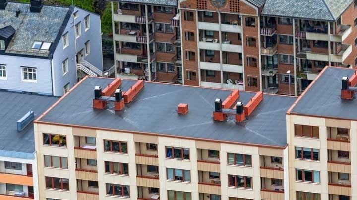 Rooftop air-conditioning units on a beige apartment building with other residential buildings in the background