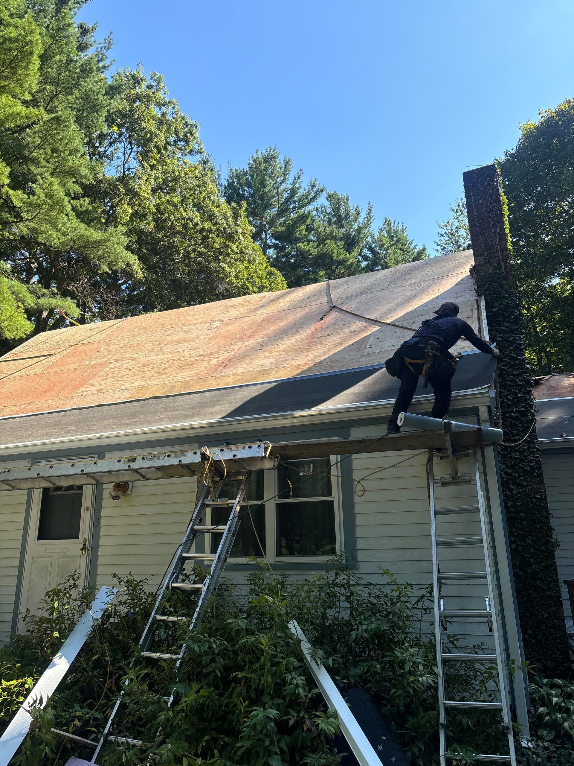 Worker on a ladder repairing a roof on a small house with peeling siding on a sunny day