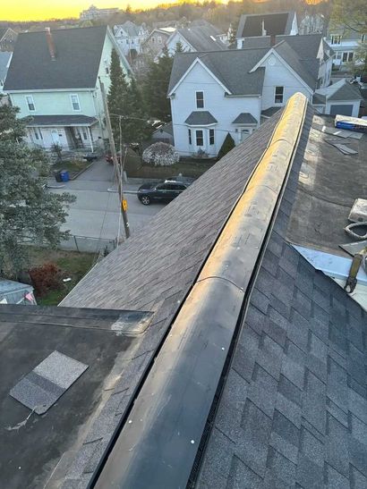 View from a rooftop ridge over residential houses at sunset, with the street and parked cars below