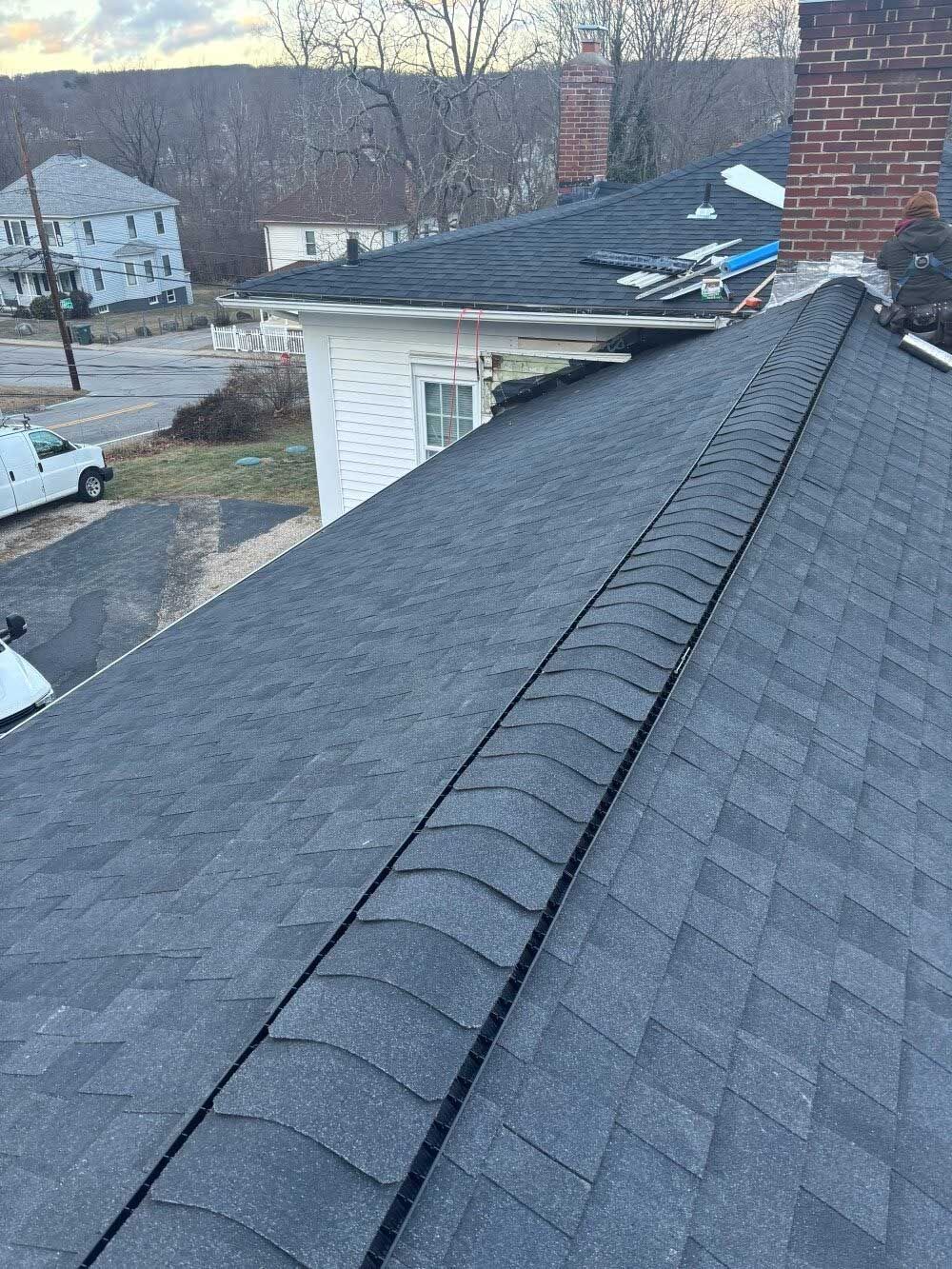 Snow-dusted roof shingles with a ridge vent and two brick chimneys on a suburban house