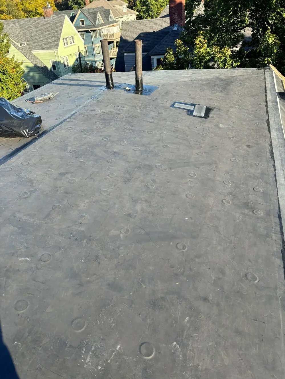 Flat rooftop with vents, overlooking nearby houses and trees on a sunny day