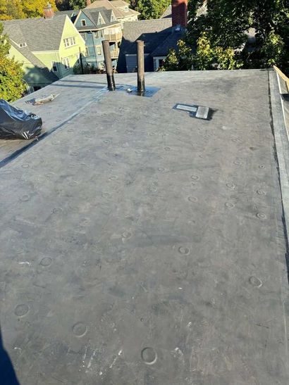 Flat rooftop with vents, overlooking nearby houses and trees on a sunny day