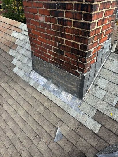 Brick chimney with a metal flashing base on a gray shingled roof