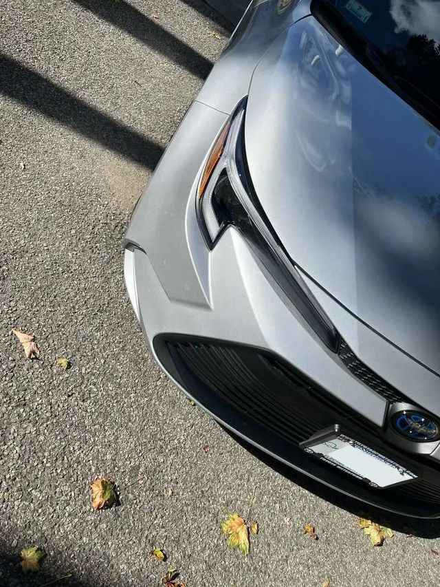 Silver car front end, with headlights and license plate, on asphalt.