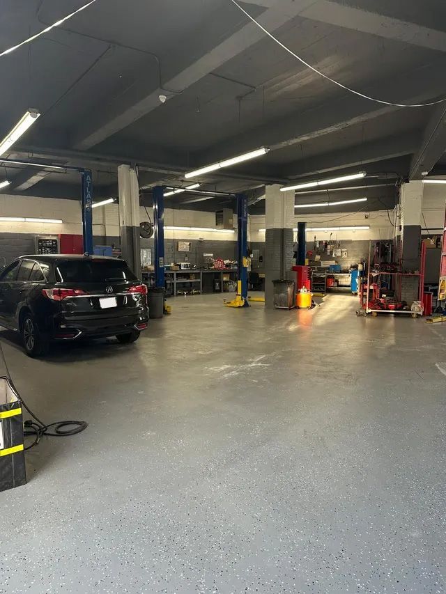 Car repair shop interior with vehicle, lift, tools, and equipment. Dark floors, and high ceilings with fluorescent lighting.