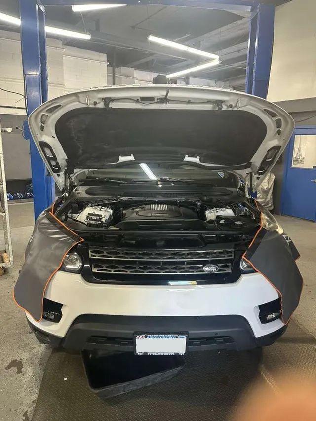 White Land Rover SUV with the hood open in a repair shop, car on a lift.