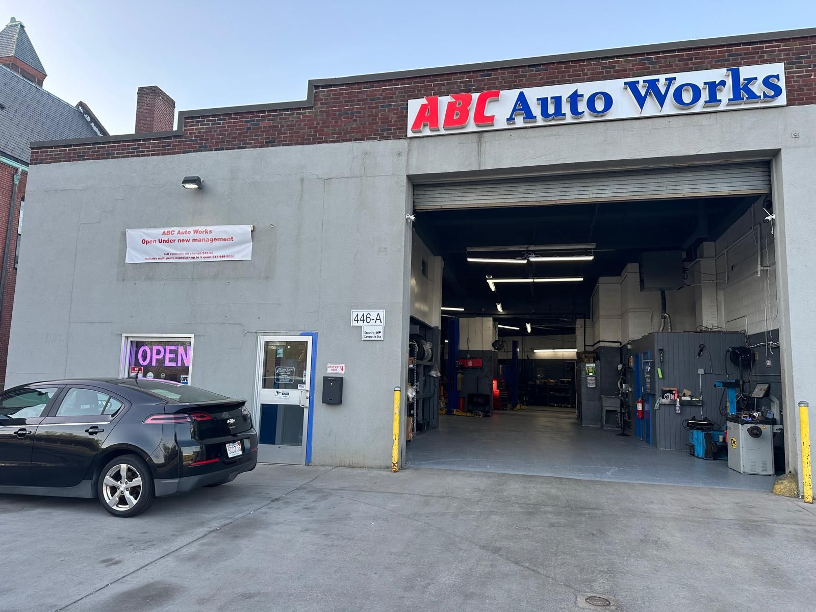 Exterior of ABC Auto Works with garage door open, black car parked in front.