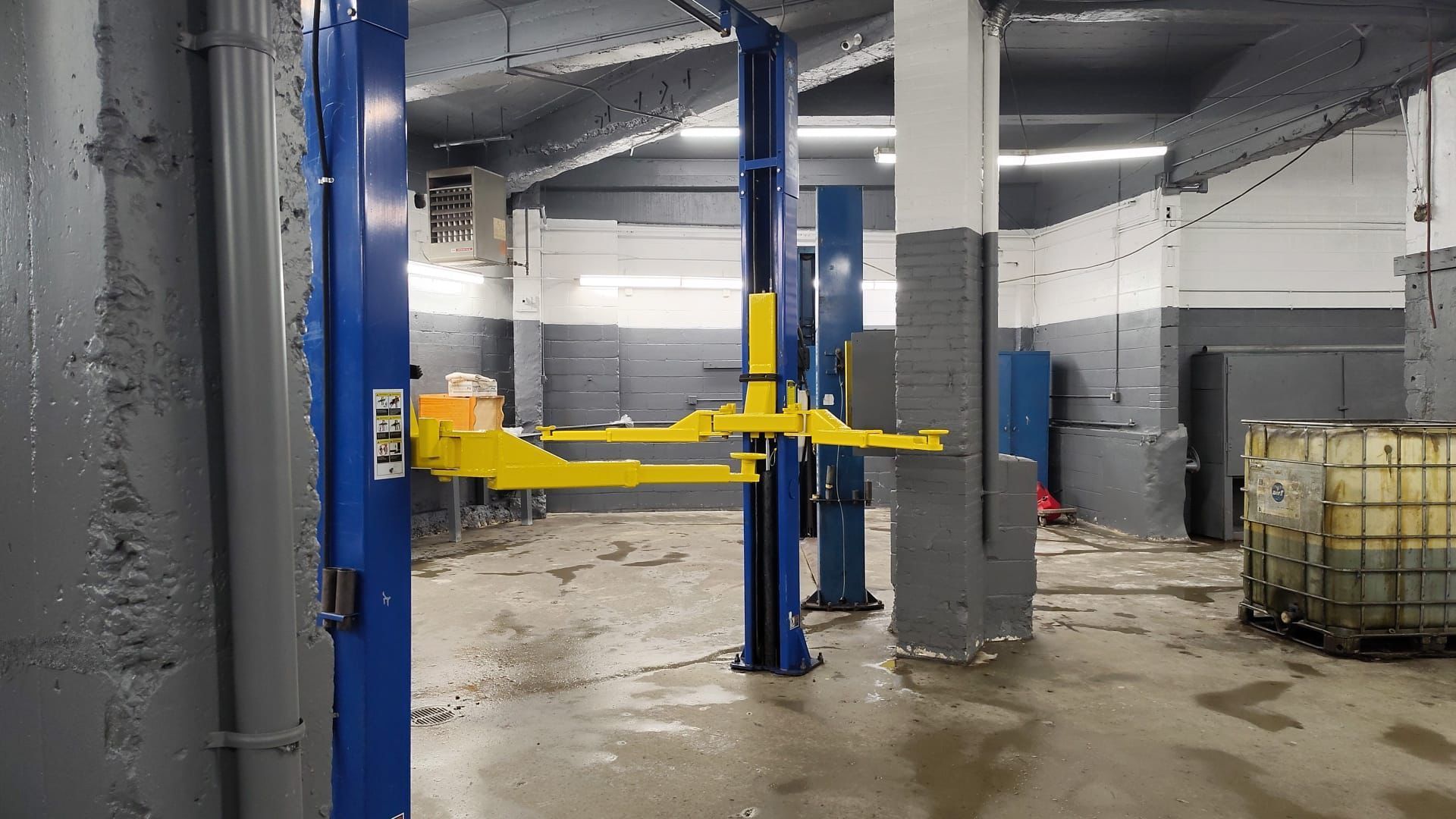 A car lift in a garage with blue and yellow lift arms, and a white, gray, and black setting.