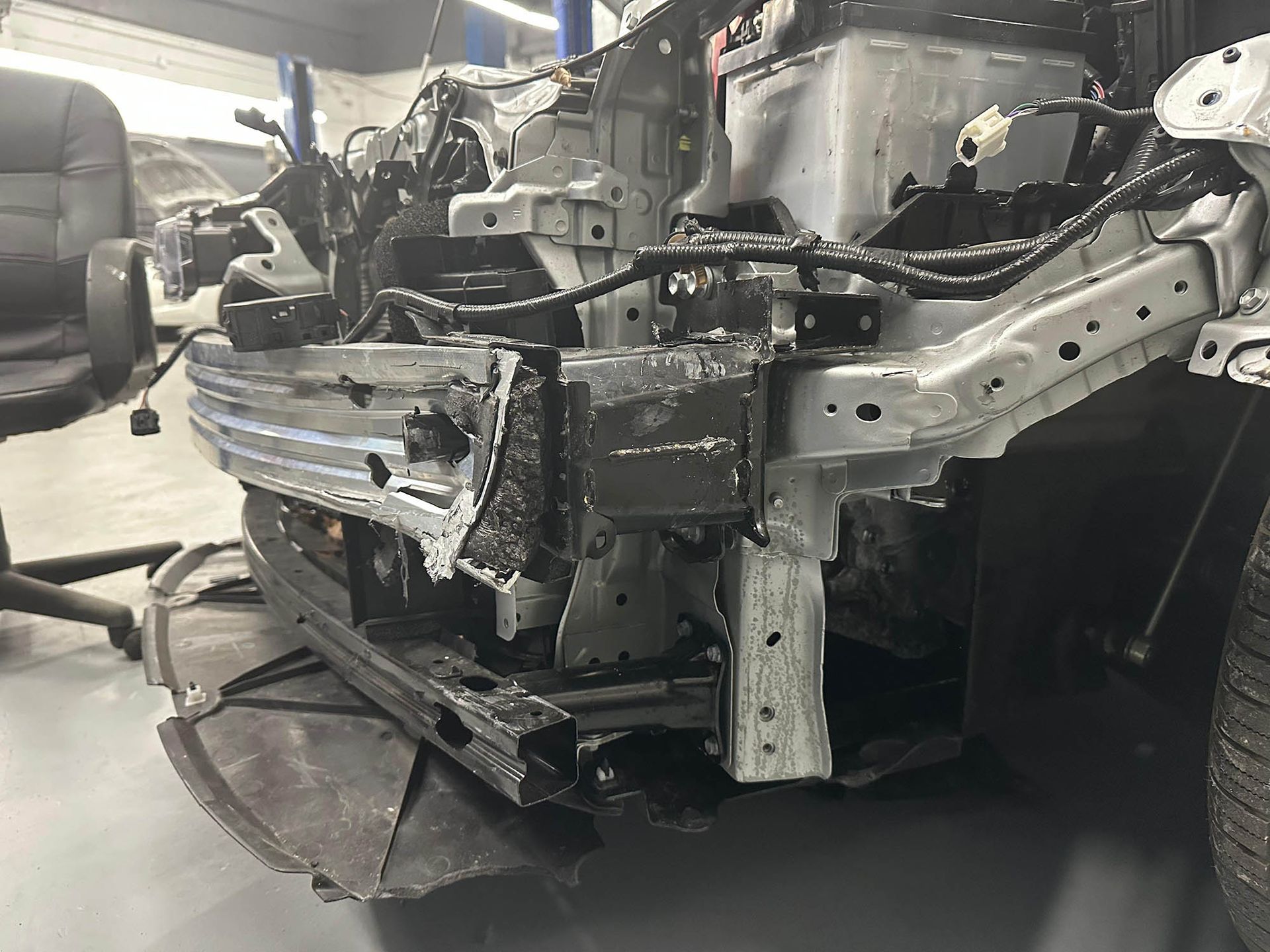 Damaged car front end with exposed frame in a repair shop.