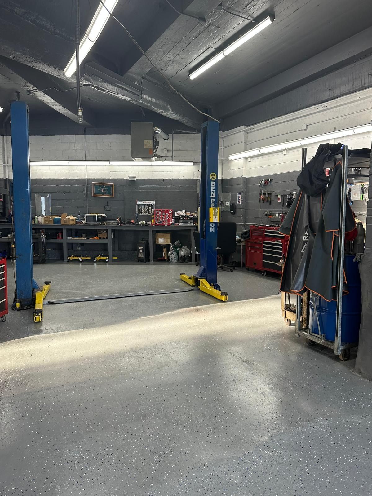 Inside a garage with a car lift, tool cabinets, and work benches.