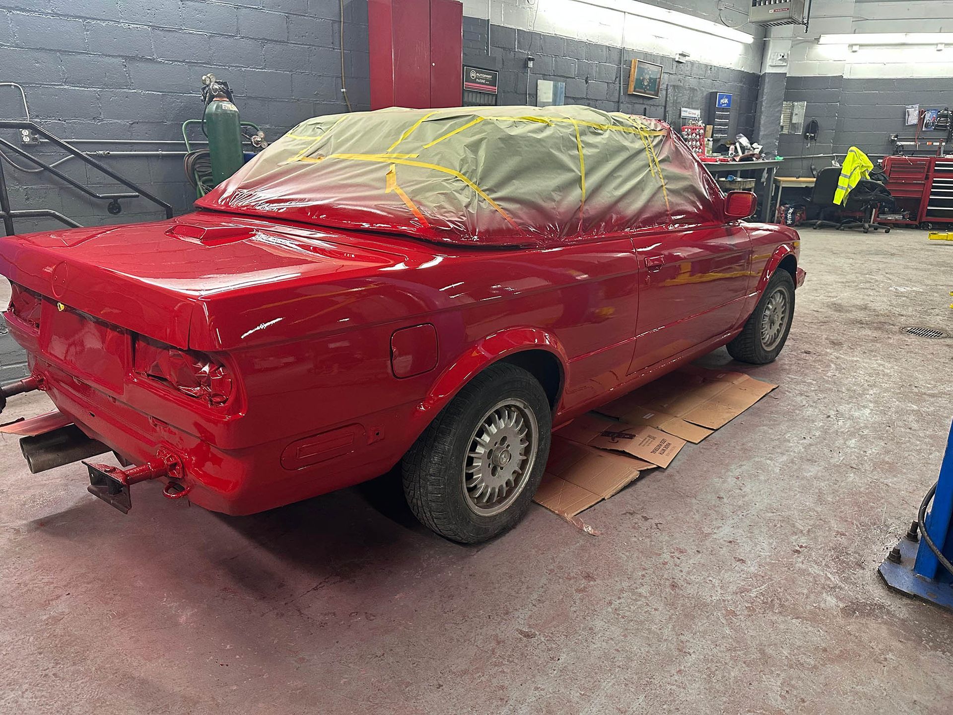 Red convertible car in a garage, taped and partly painted.