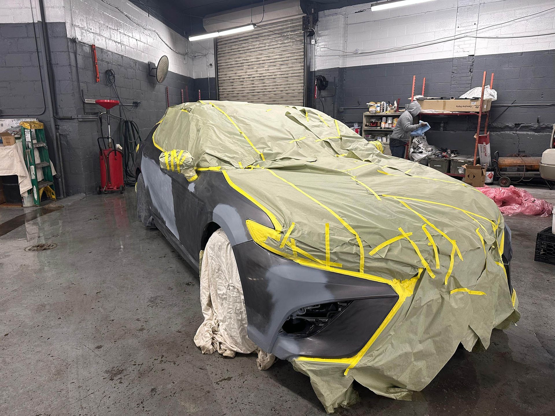 Car covered in masking paper and tape, in a garage, prepared for paint.