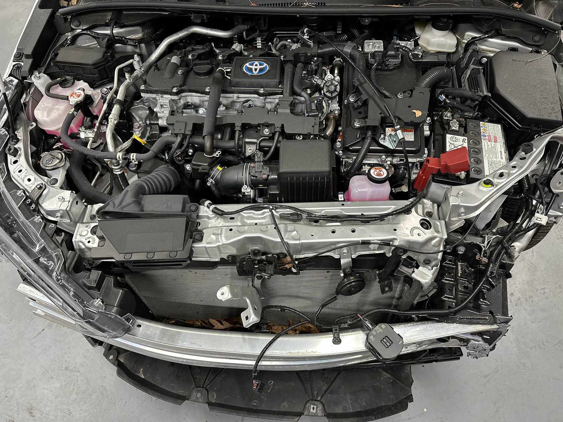 Engine bay of a silver car, visible components, including air intake and fluid reservoirs, showing damage to the front.
