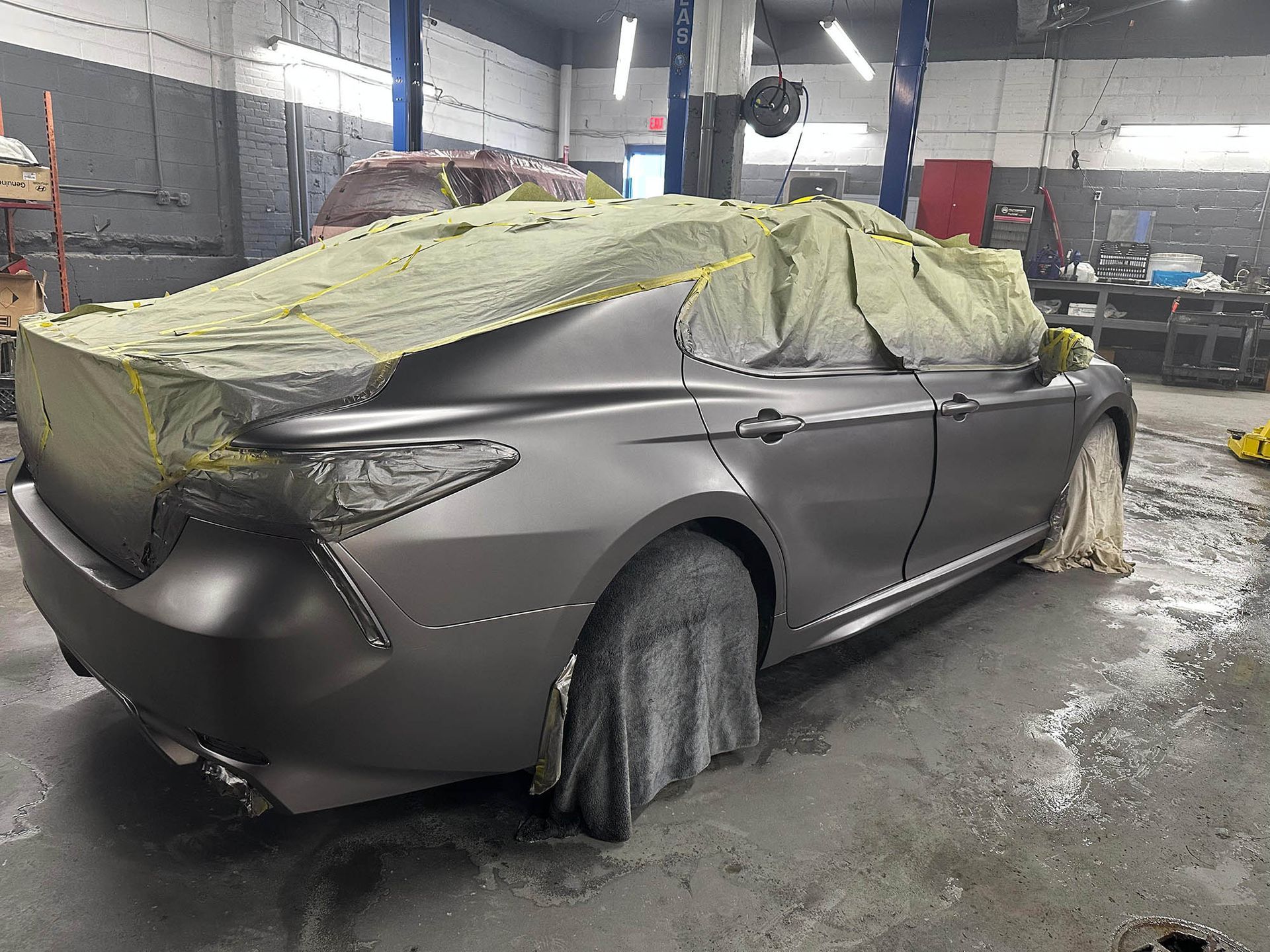 Gray car in a repair shop, partially covered with protective coverings, ready for paint.