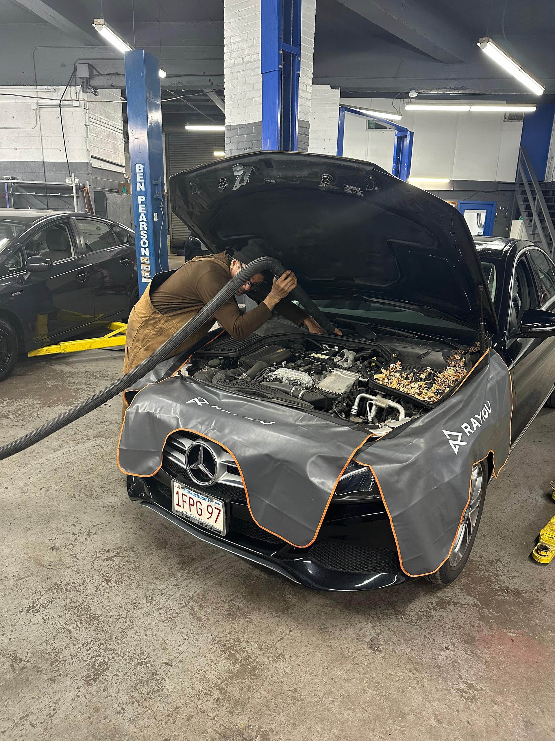 Mechanic cleaning a car engine with a hose in a repair shop.
